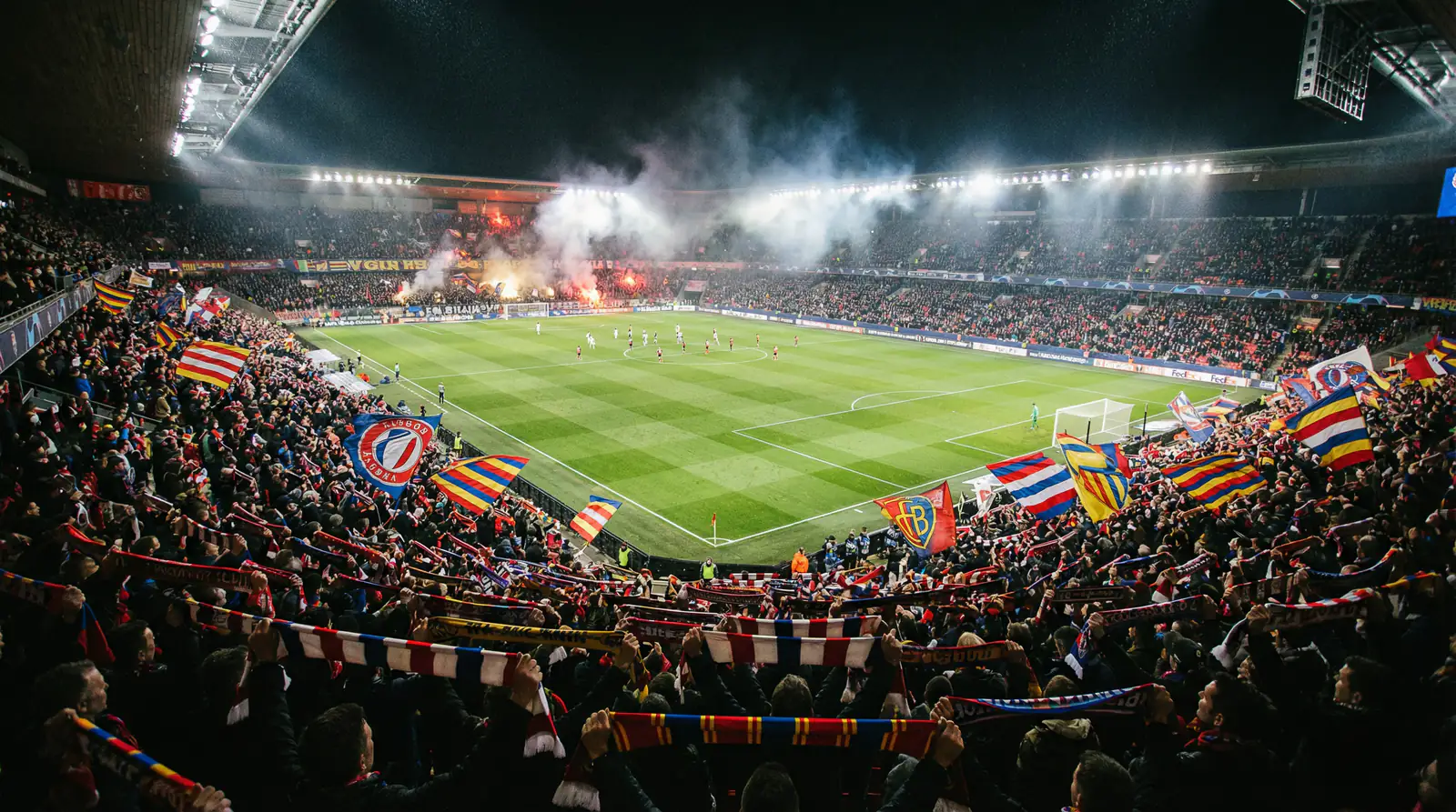 Estadio de fútbol lleno de aficionados animando con bufandas y banderas visto desde la grada